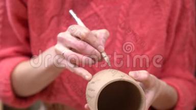 女陶工的特写，用刀子在她手中的生泥杯上装饰。